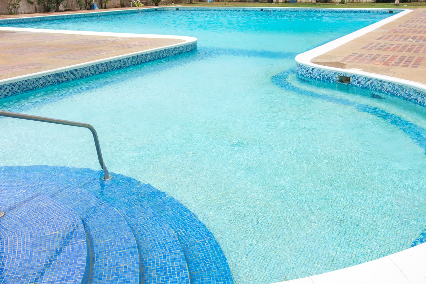 Una piscina blu vuota con gradini piastrellati e un solarium.